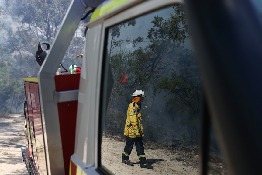 A firefighter is seen reflected in a vehicle window as New South Wales Rural Fire Service personnel conduct a controlled burn