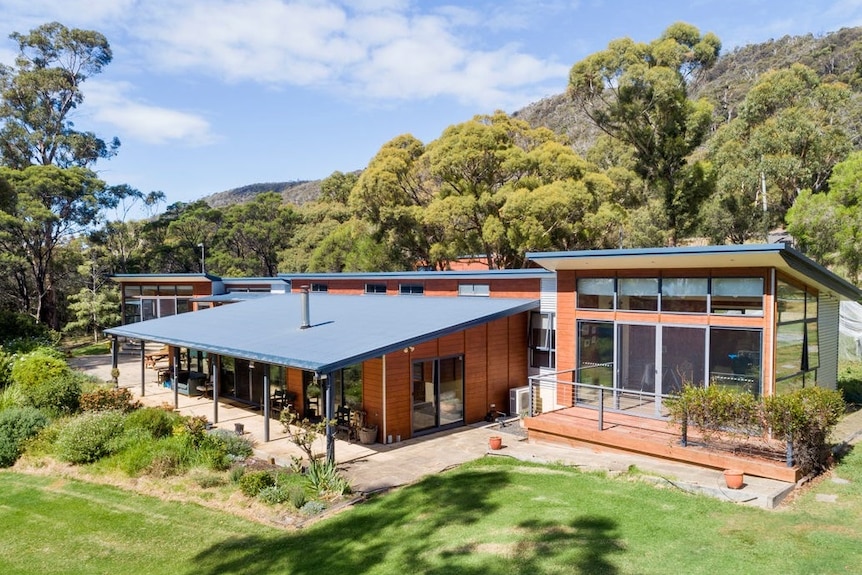 Blue steel rooves cover a home comprised of multiple structures nestled in bushland.
