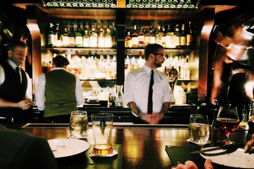 Bartenders working behind a dimly-lit, upscale bar