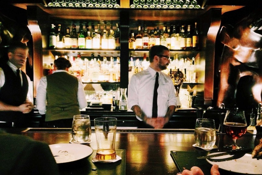 bartenders working behind a dimly-lit, upscale bar