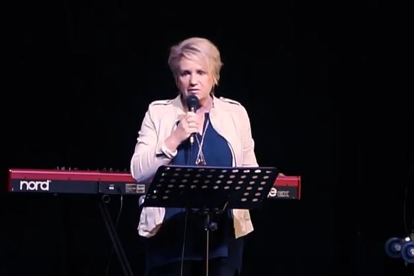 A woman standing on a stage speaks into a microphone.