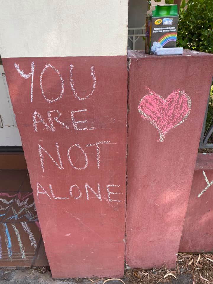You are not alone with a red heart written in chalk on a wall.