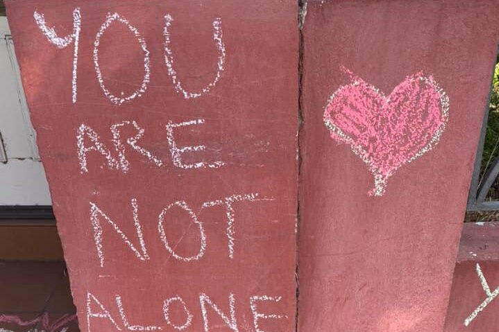 You are not alone with a red heart written in chalk on a wall.