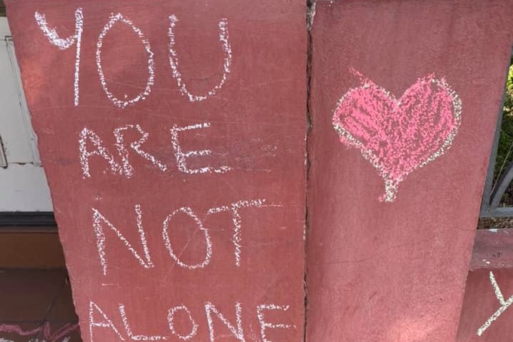 You are not alone with a red heart written in chalk on a wall.