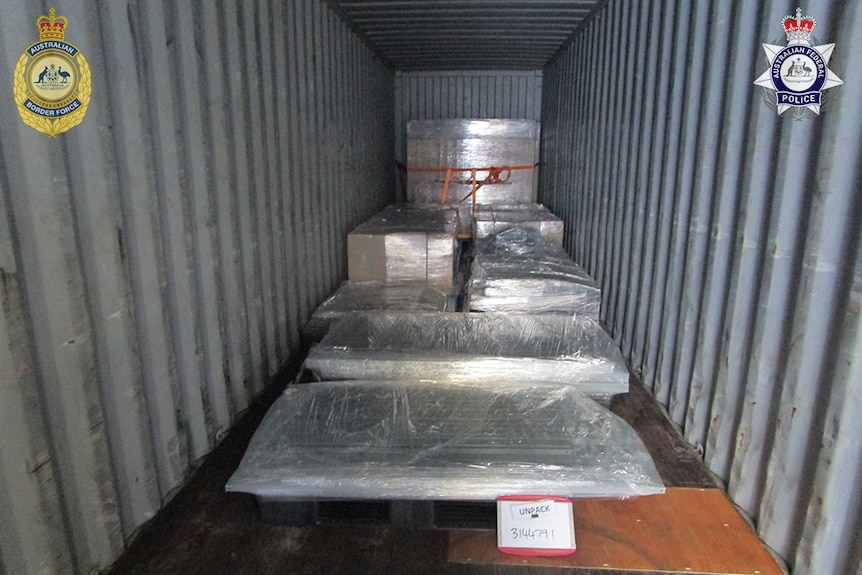 large plastic-wrapped packages inside a shipping container with police watermarks on the photo