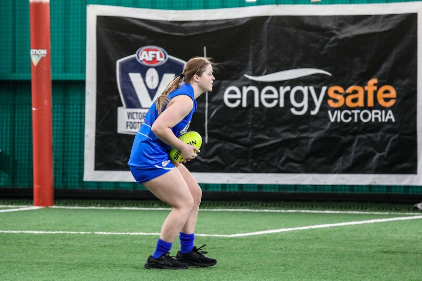 Courtney holds a football while on an indoor football field.