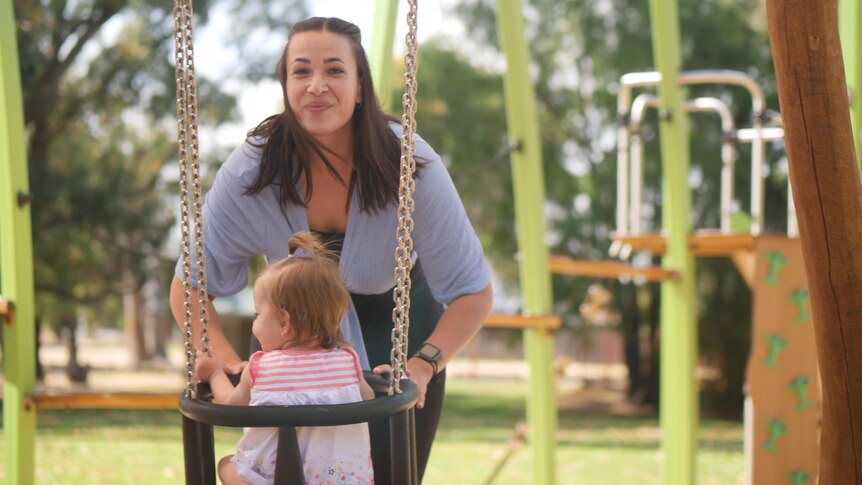 A woman pushing her daughter on the swing. 