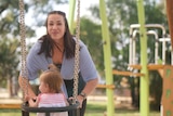 A woman pushing her daughter on the swing. 