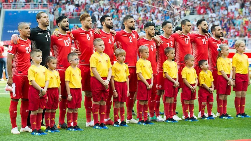A male soccer team wearing all red lines up with mascots before a big game