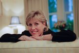 A woman smiles into the camera with her arms folded on the back of a lounge