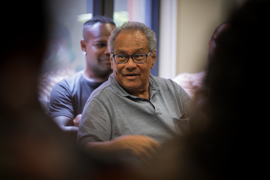 Older Torres Strait Islander man in a grey shirt sitting at a theatre rehearsal.