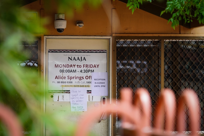 The front door of a reddish building with a white sign on the board reading 'NAAJA'