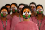 Young with the colours of the Indian national flag painted on their faces wear red tops and stare at the camera as they pose.