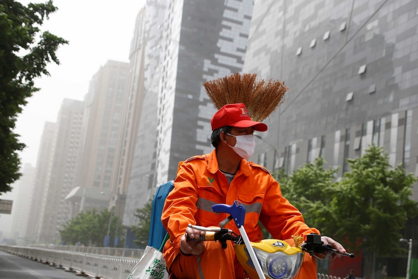 A street cleaner wears a face mask as he rides a scooter.