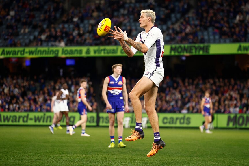 A Fremantle forward with a shock of blond hair leaps up to catch the ball.