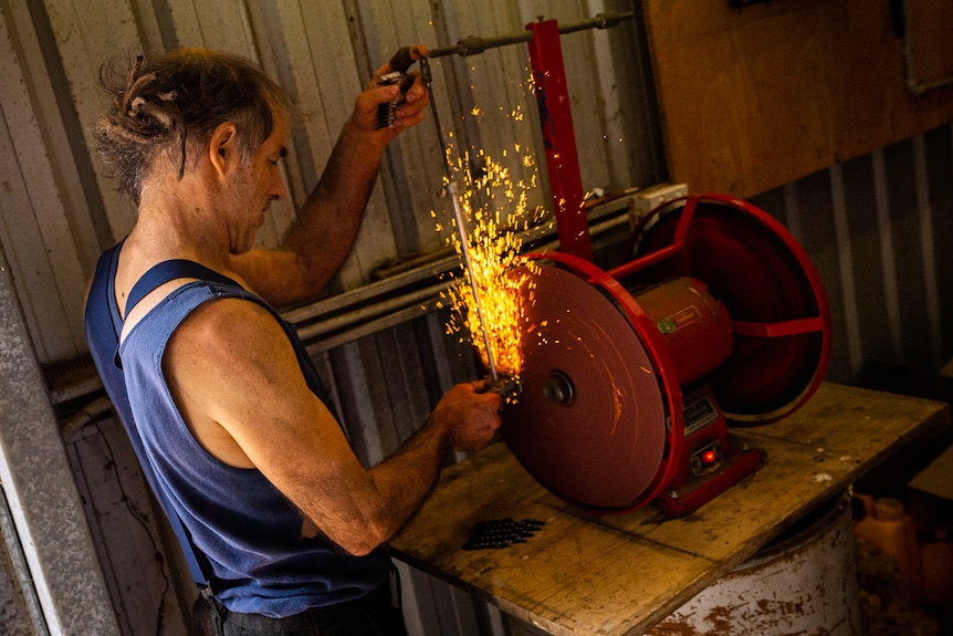 Photo of a man sharpening a shearing tool.