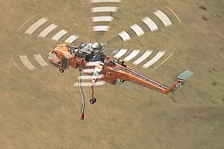 A water bomber flies above the ground.