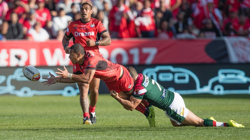 William Hopoate of Tonga offloads a pass under the tackle of Robbie Farah.
