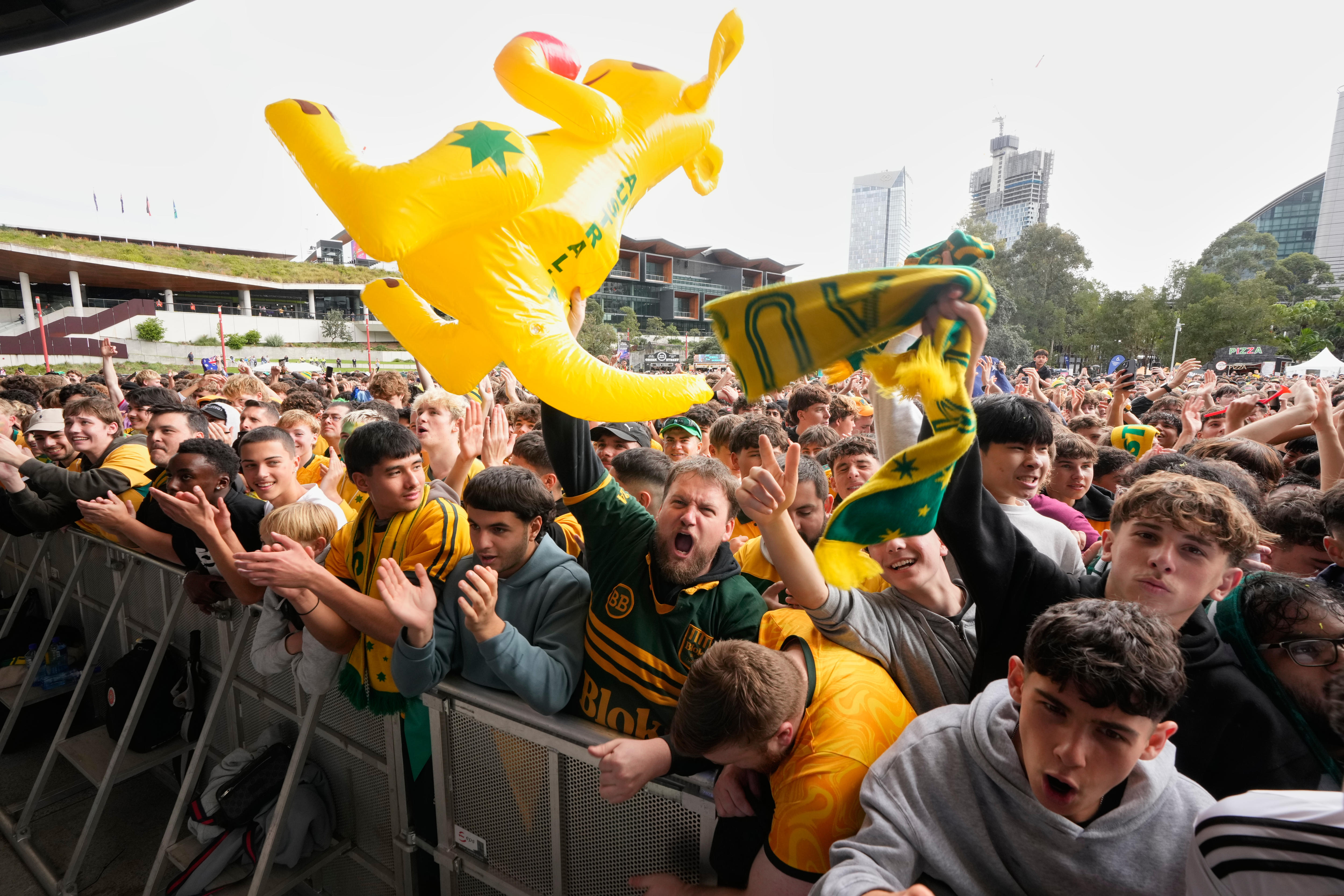 A large crowd, many wearing Socceroos jerseys. One holds up an inflatable kangaroo.