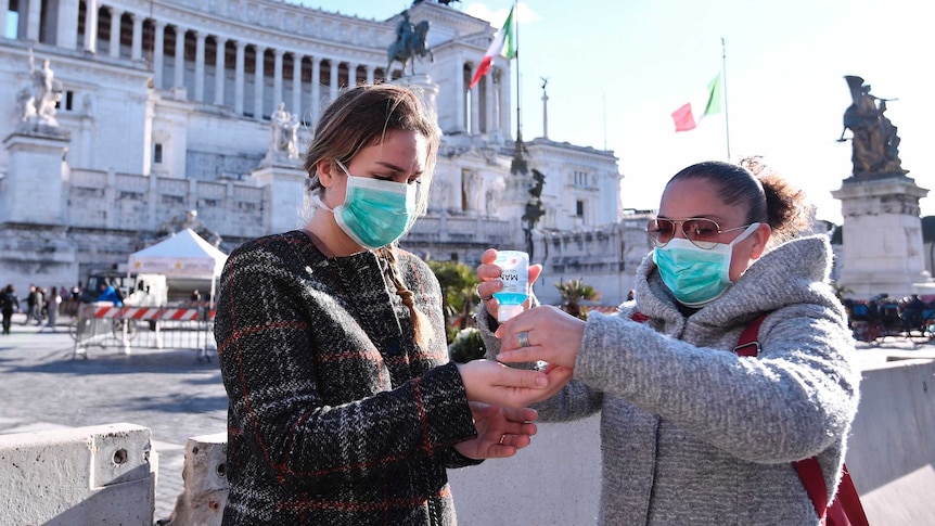 Женщины в масках дезинфицируют руки посреди площади Пьяцца Венеция.