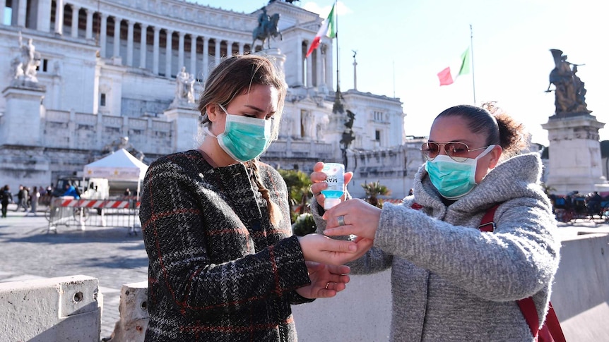 Women wearing face mask disinfect their hands in central Piazza Venezia.