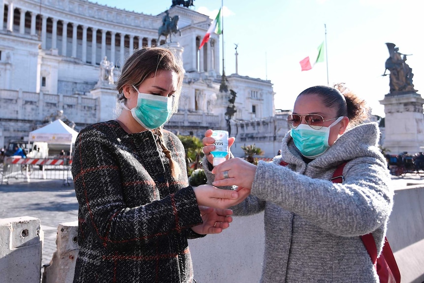 Women wearing face mask disinfect their hands in central Piazza Venezia.