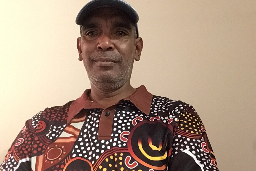 A man wearing a cap and polo shirt decorated with Aboriginal art smiles at the camera
