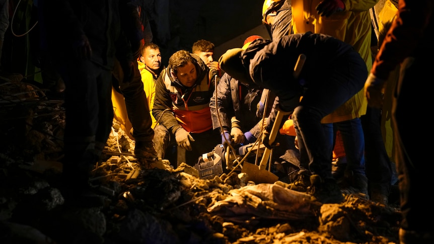 A group of people frantically dig at rubble at night