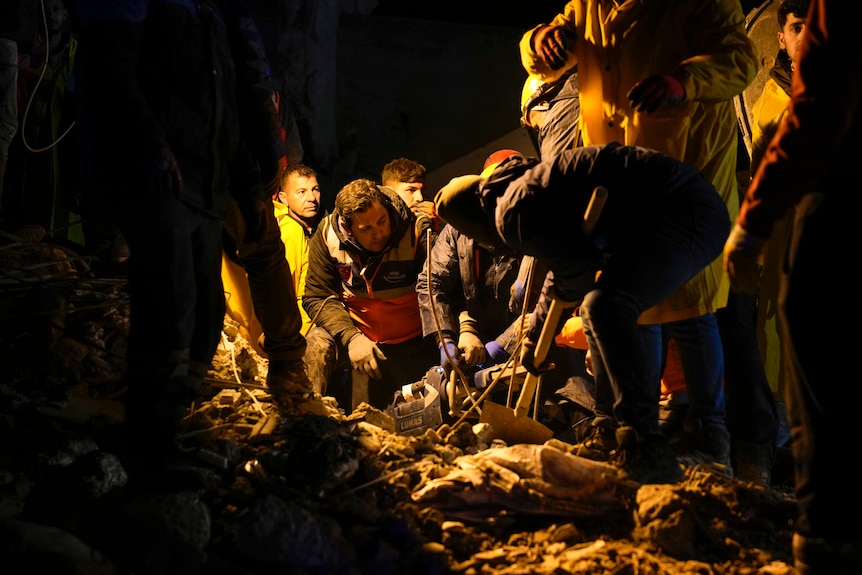 A group of people frantically dig at rubble at night