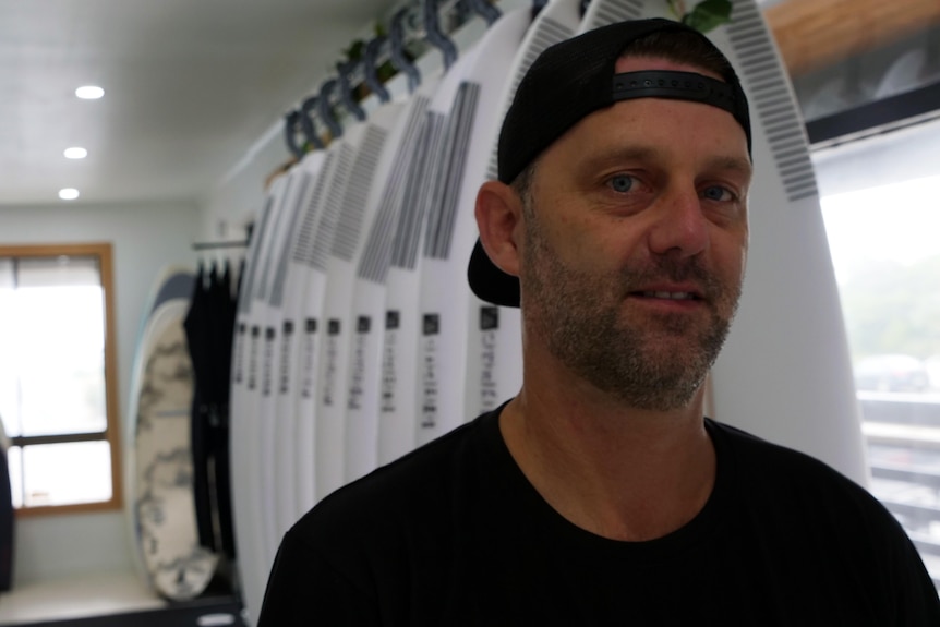 man in baseball cap standing in front of surfboards