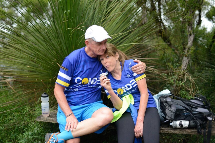 Man and woman in matching blue Condev shirts, sitting on a bench hugging after a hike.