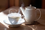 A steamy hot cup of tea next to a teapot