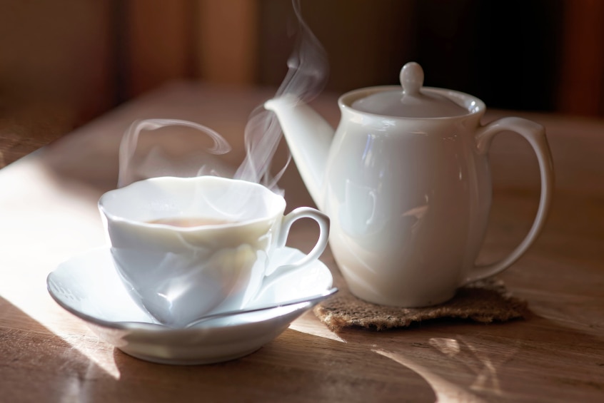 A steamy hot cup of tea next to a teapot