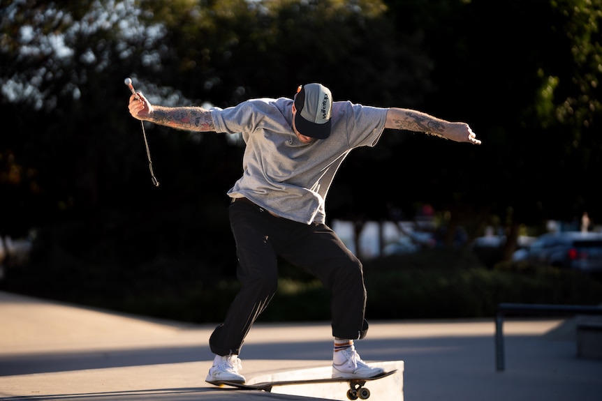 Richard Moore on his skateboard with his arms out wide, a cane in one hand