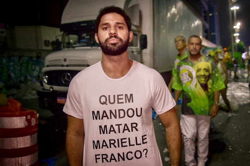 A man looks at the camera and shows a message written on his shirt
