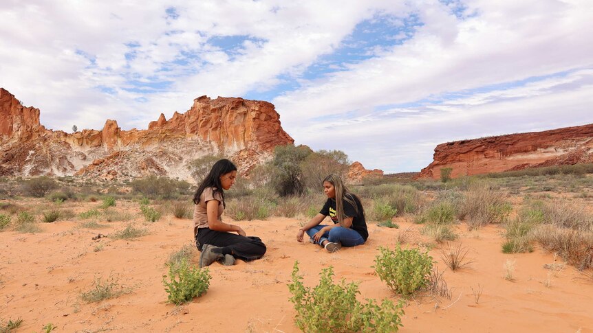 Two Aboriginal woman sitting on the ground at Rainbow Valley.