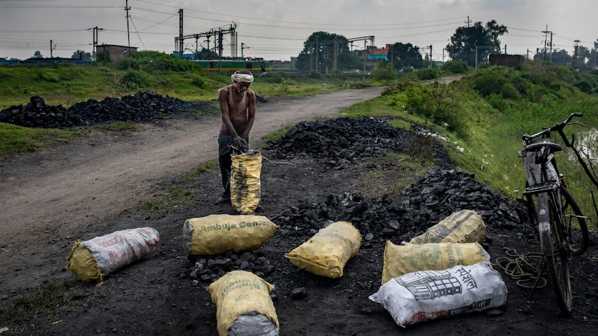 A slim Indian man fills scavenged coal into sacks at dusk on open coal mine