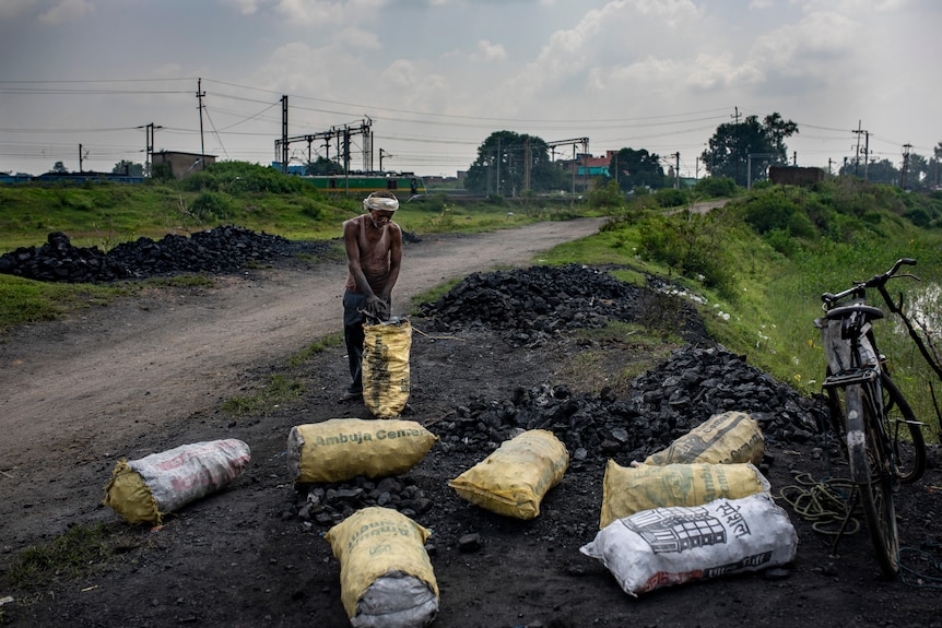 A slim Indian man fills scavenged coal into sacks at dusk on open coal mine