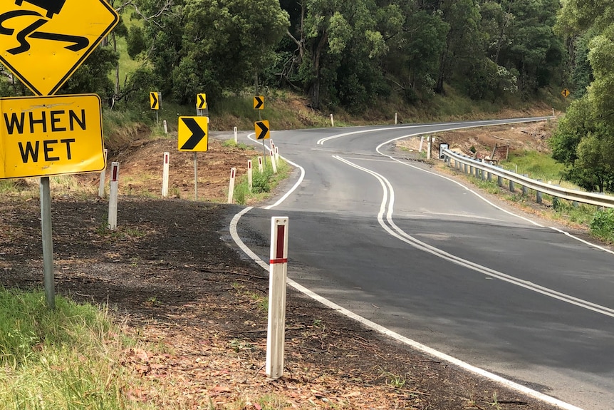 Curved country road with a landslip and road signs visible