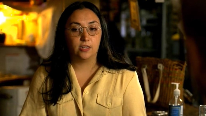 A woman in a light blouse and glasses sits in front of an empty bar.