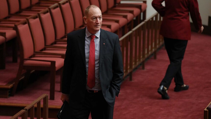 Anning is walking, hand in pocket, wearing a suit with a red tie and stripy shirt.