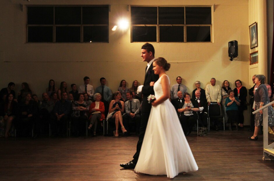 A young man and woman walk across a wooden dance floor.
