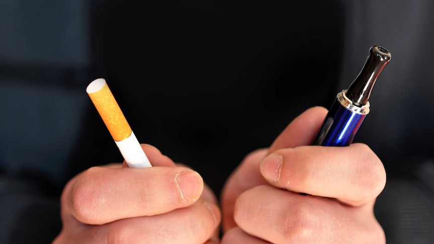 A person holds a tobacco cigarette in one hand and an electronic cigarette in the other.