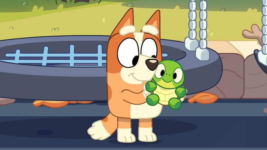 A small, ginger animated dog holds a toy turtle.