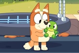 A small, ginger animated dog holds a toy turtle.
