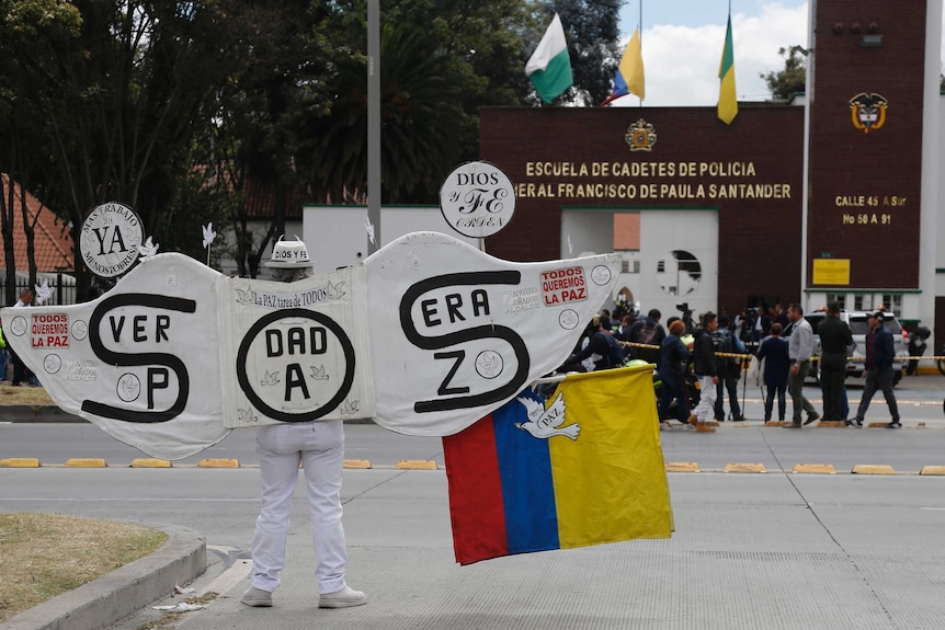 A man outside the police academy is seen wearing large angel wings that read in Spanish: "S.O.S. True Peace".