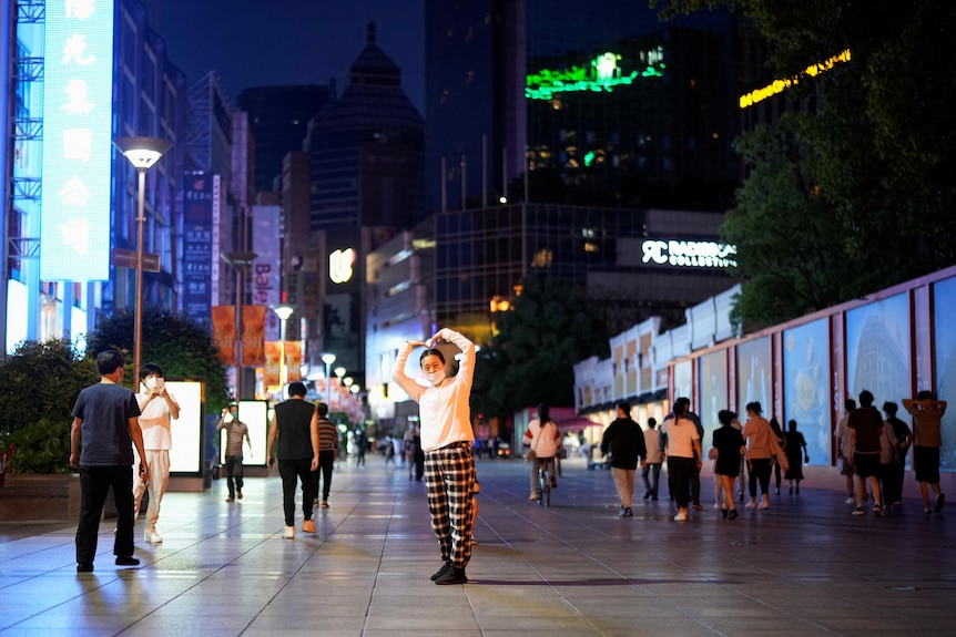 A woman poses for pictures at a main shopping area at night. 