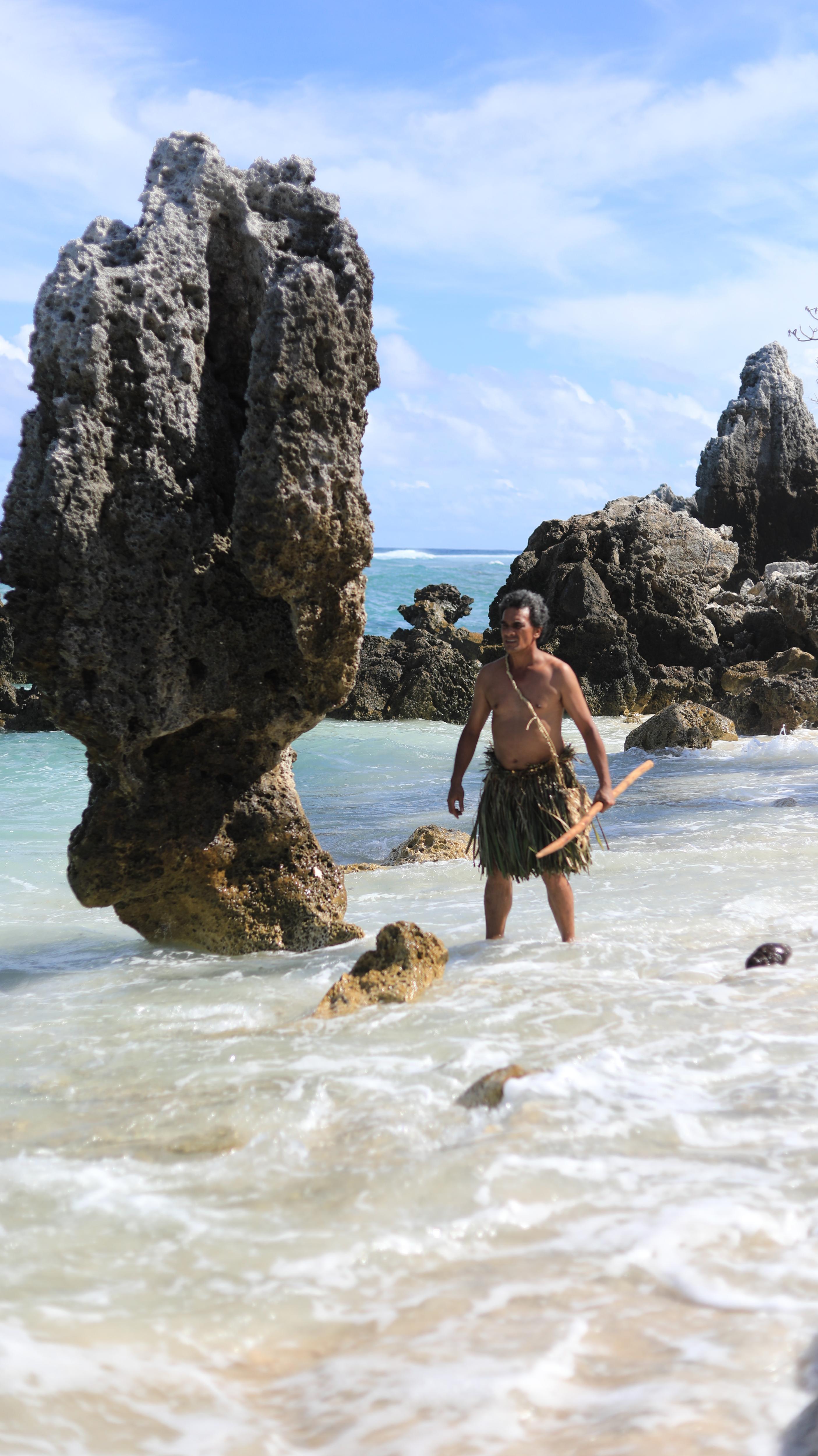 A man stands amongst rocks in the ocean.