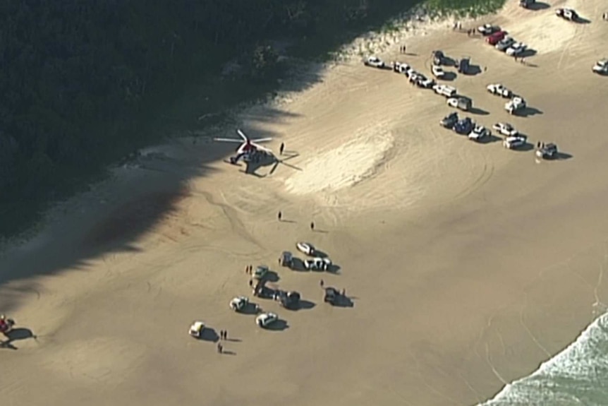 An aerial view of a beach with multiple vehicles including helicopters.