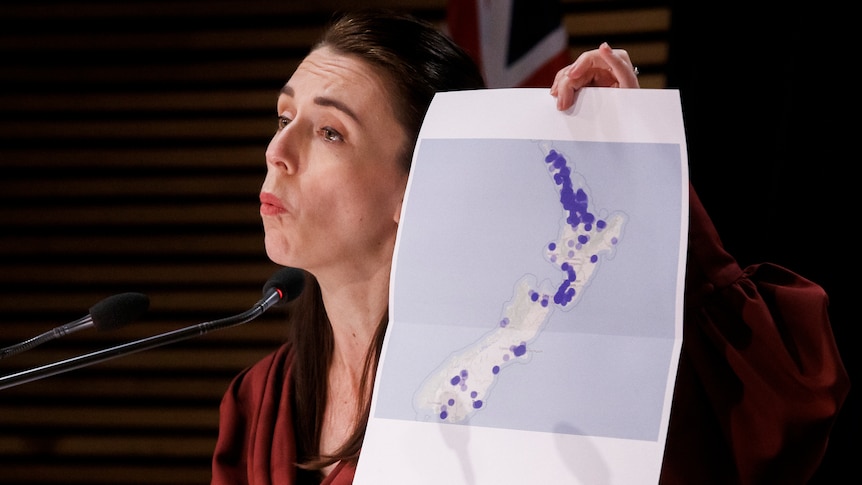 New Zealand Prime Minister Jacinda Ardern holds a map with blue dots on it. 